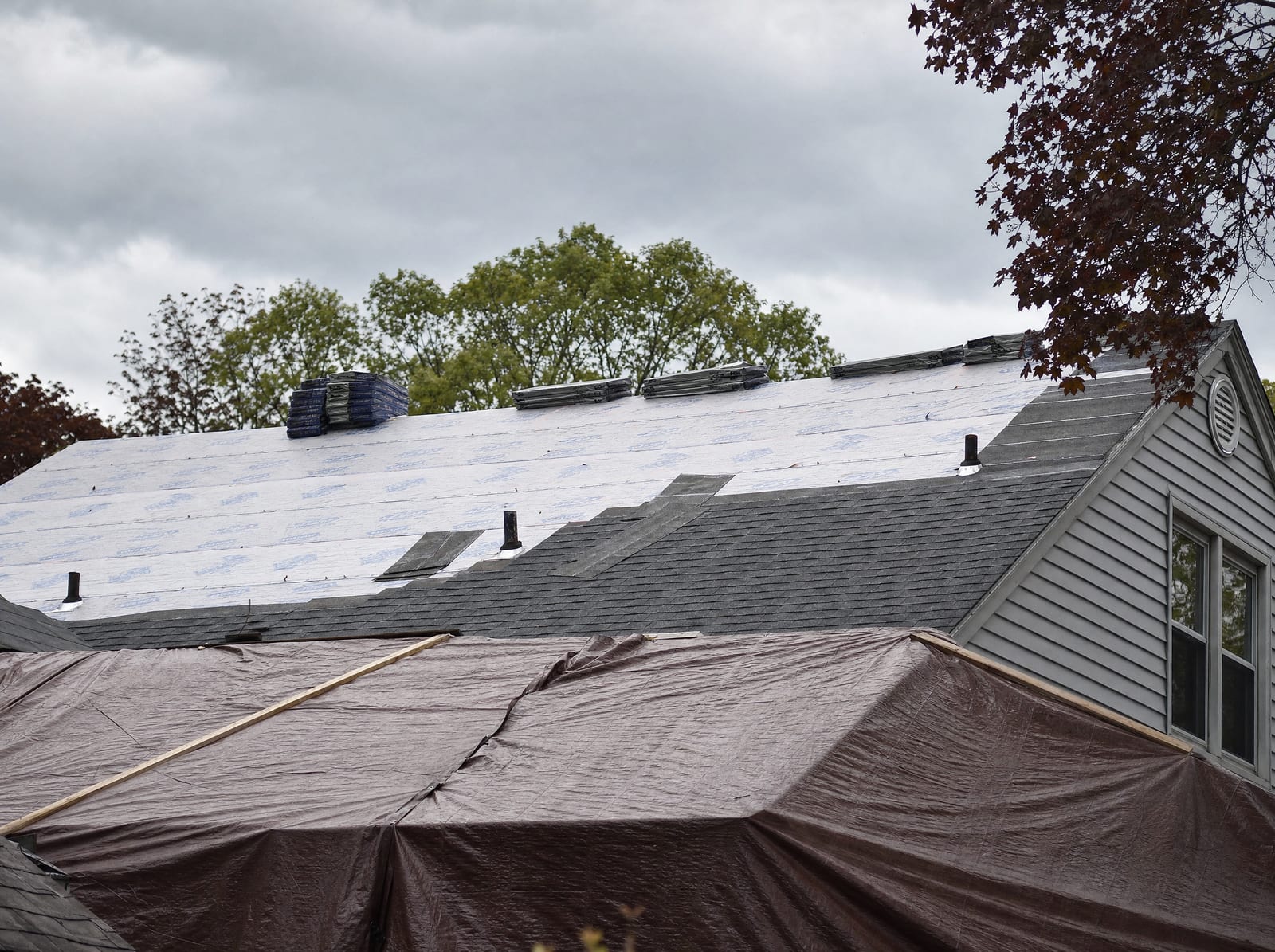 New shingles going on over underlayment while part of the roof stays tarped against the weather