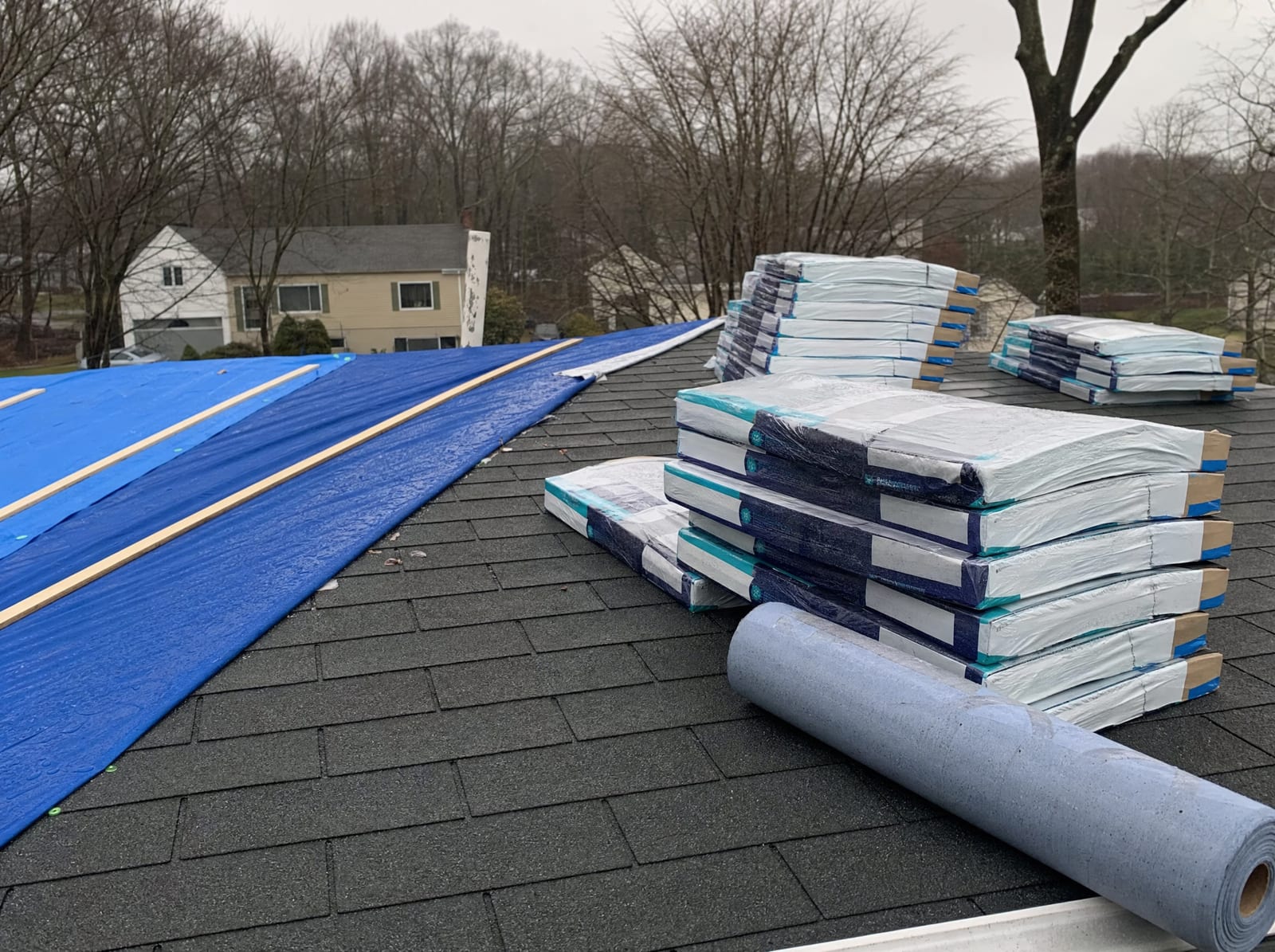 Roofing shingle bundles and underlayment staged on a roof with a section tarped ahead of incoming weather