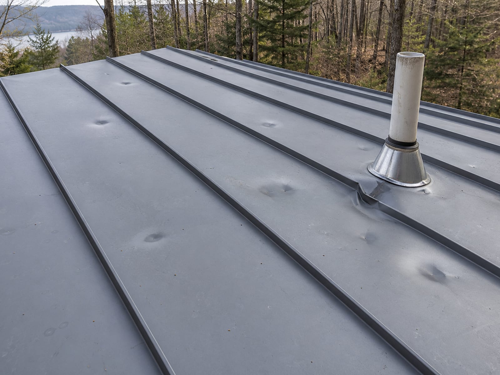 Standing seam metal roof panels with round dents, one dent touching a raised seam beside a roof vent