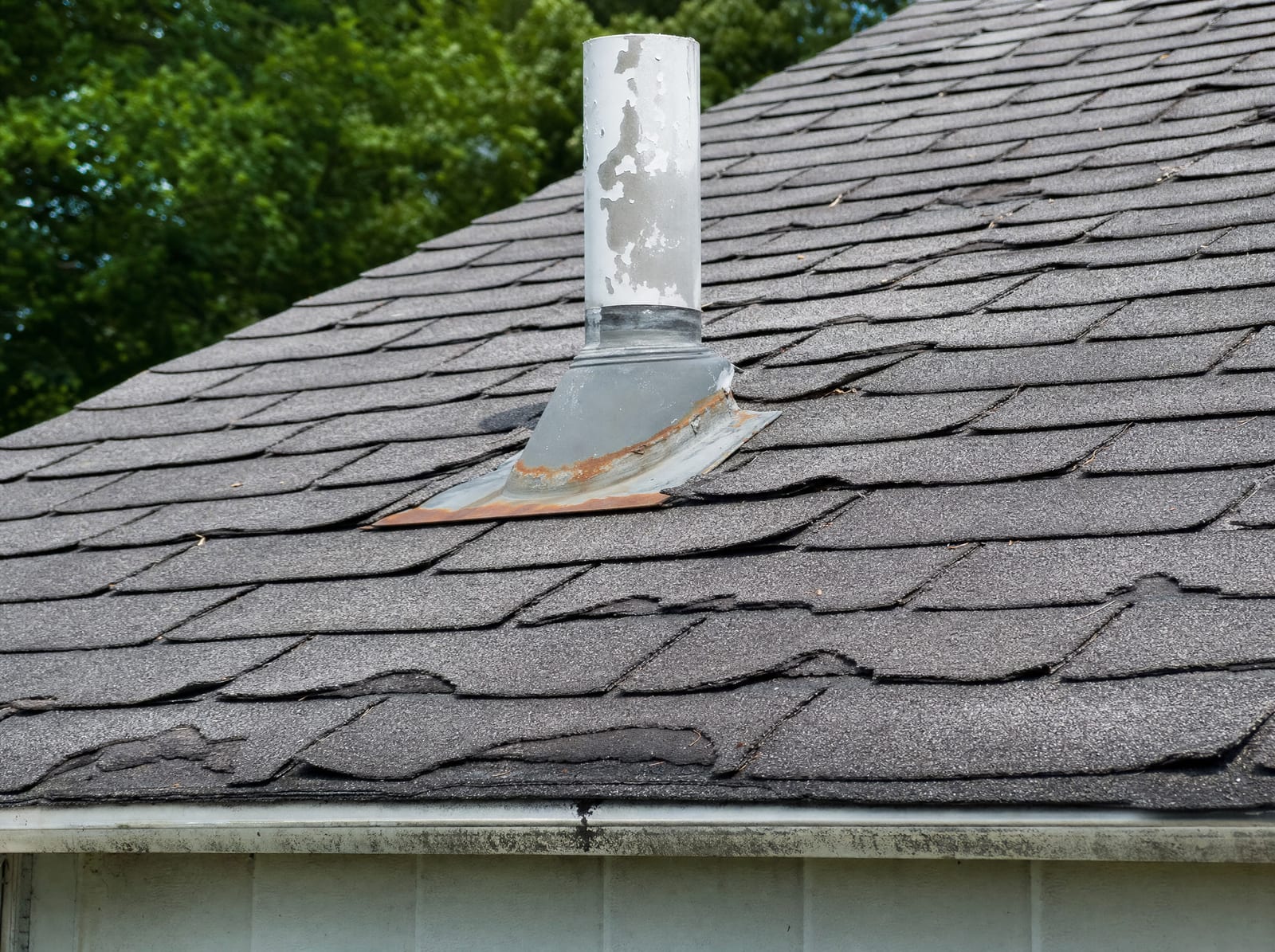 Close inspection of a worn residential roof showing curling shingles and aging flashing