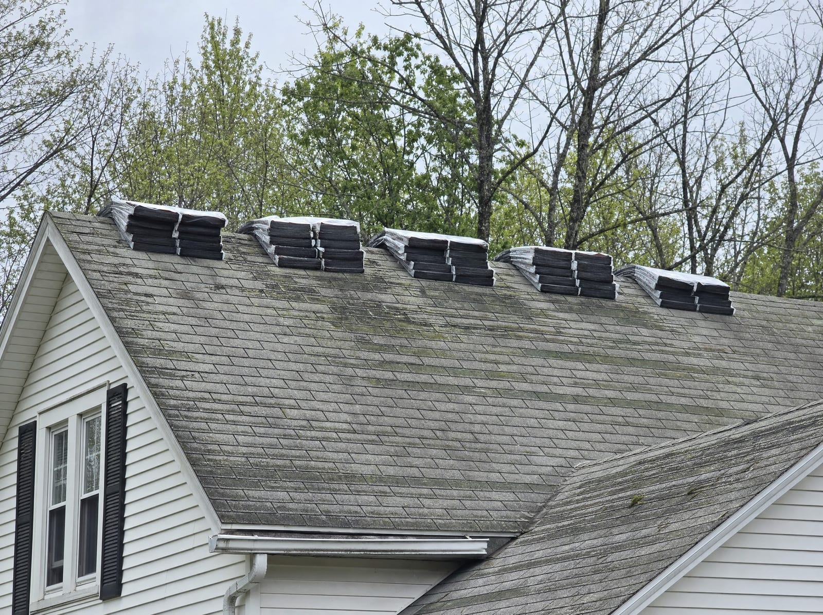 New shingle bundles staged on top of an existing aged shingle roof before an overlay