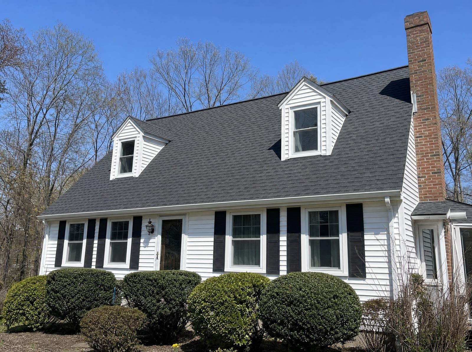 Completed overlay roof with a uniform fresh shingle surface on a Cape-style home