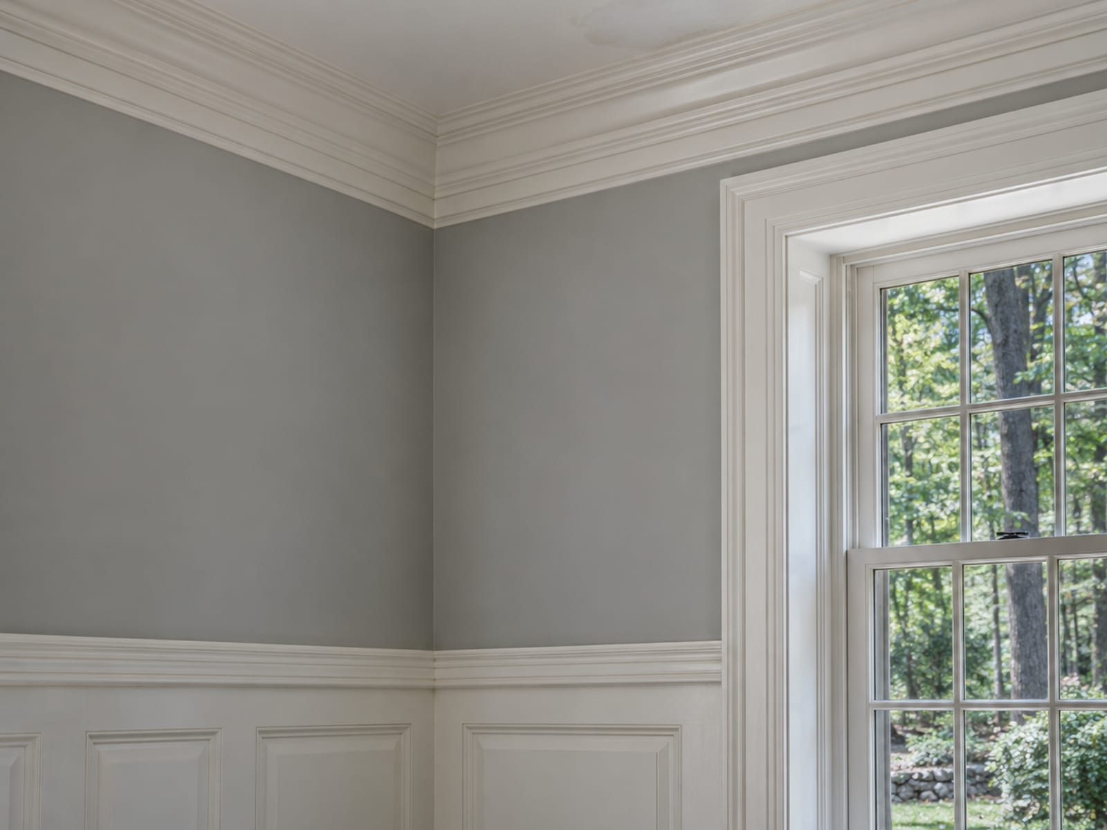 Corner of a tall room with painted crown molding, paneled wainscot and a small patched and primed area on the ceiling edge
