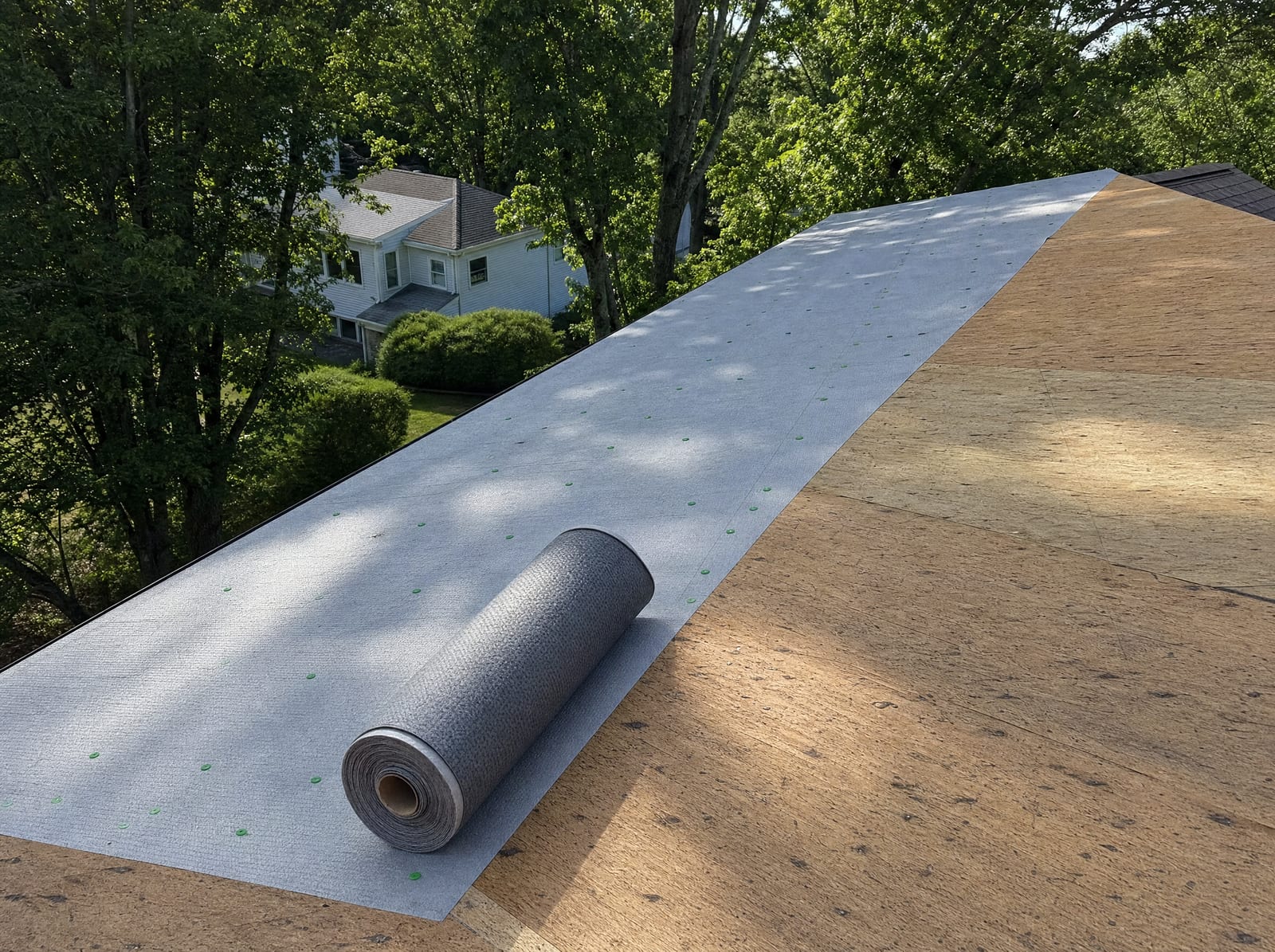 Synthetic underlayment rolled out over fresh plywood decking on a ranch roof