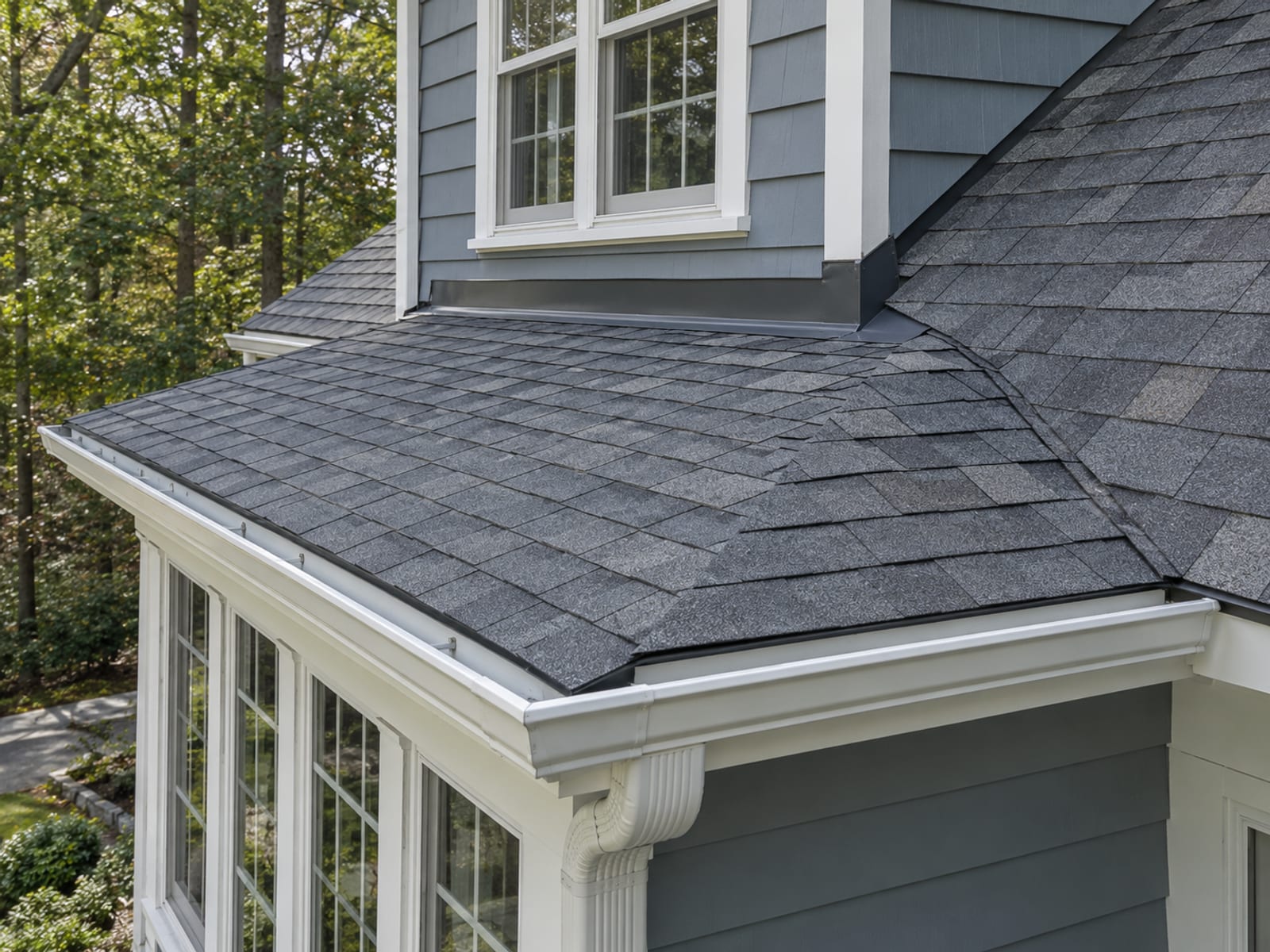 Finished low slope roof over a porch tied into a shingle roof with new flashing, a window corner and clean gutters