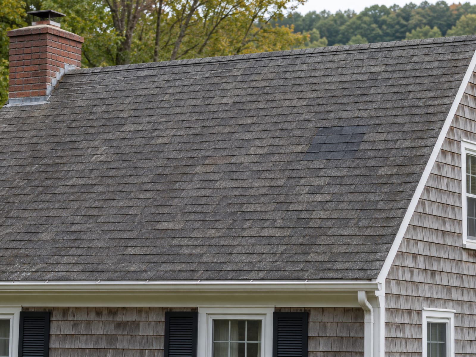 Older asphalt shingle roof with one small patch of newer, slightly darker shingles near the ridge on an otherwise sound roof slope