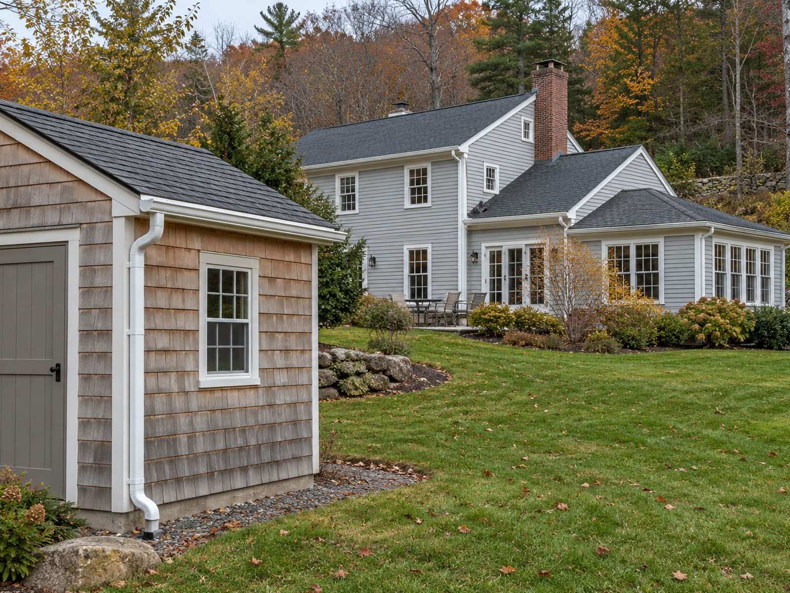 Small garden shed with a short gutter showing coupler seams in the foreground and a colonial with an addition and a multi-corner white gutter line behind it