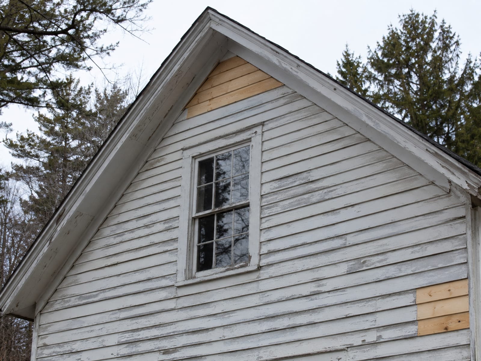 Gable end of an older house where a few new unpainted boards sit among weathered painted clapboards