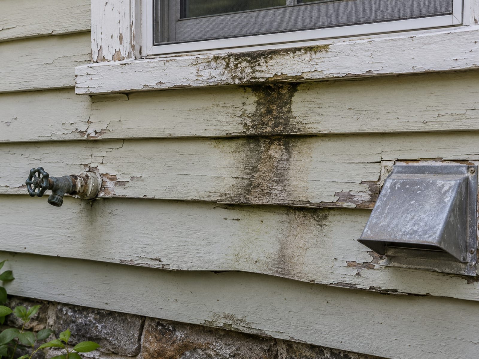 Painted clapboard wall with a stained, bowed lower board under a window sill beside an outdoor hose bib and a dryer vent hood