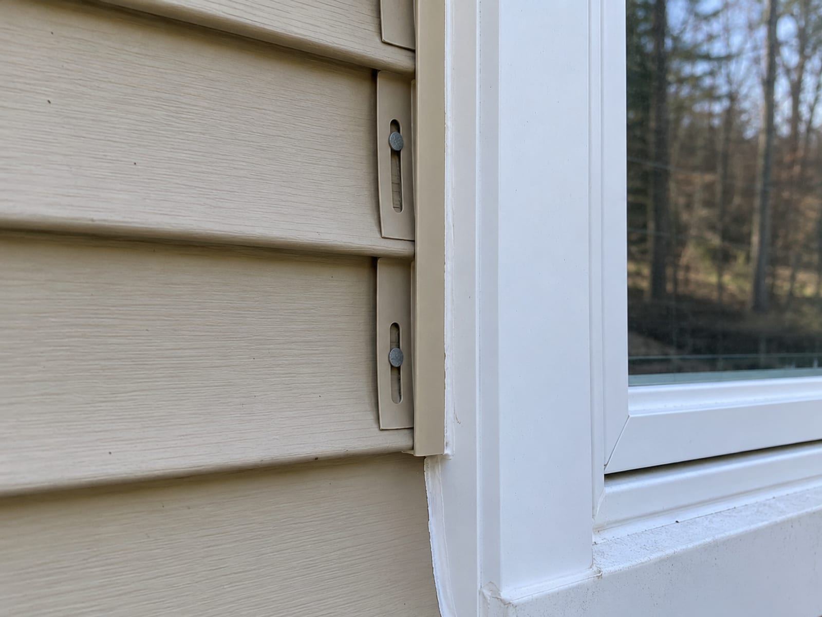 Close view of vinyl siding meeting a window with J channel, cleanly cut panel ends and centered nails