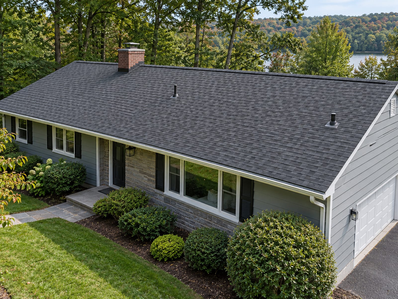Postwar ranch house with a freshly installed charcoal architectural shingle roof, clean ridge cap and tidy gutters on a mown lawn