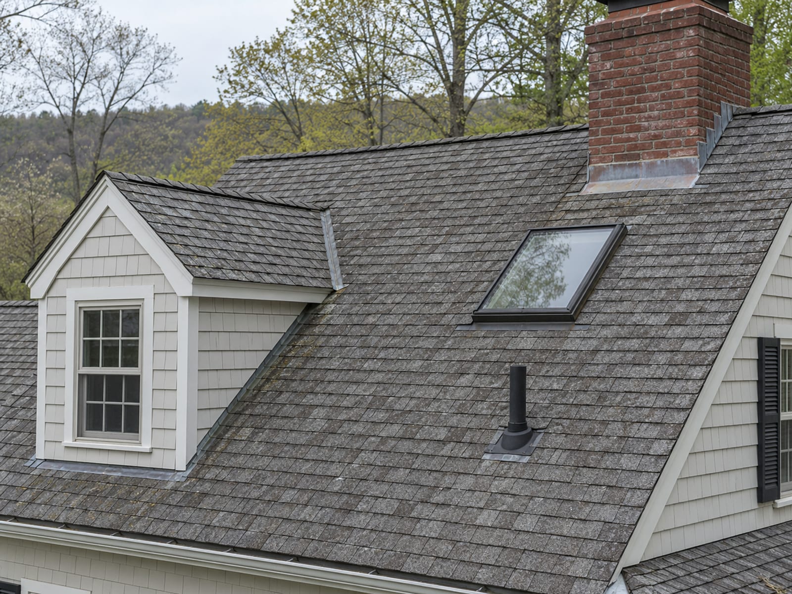 Gray shingle roof with a dormer, a skylight, a brick chimney with flashing and a plumbing vent pipe on the same slope