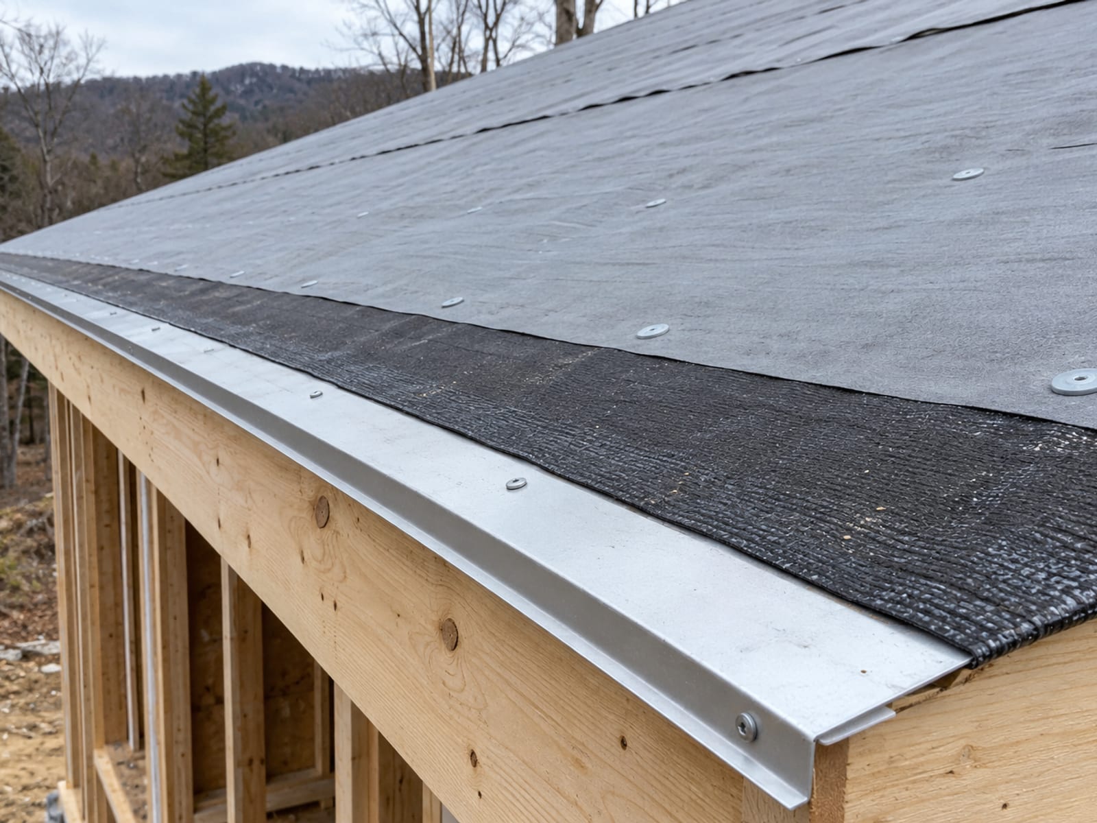 Low angle view of a roof eave with metal drip edge, black ice and water membrane and gray underlayment laid over bare plywood decking