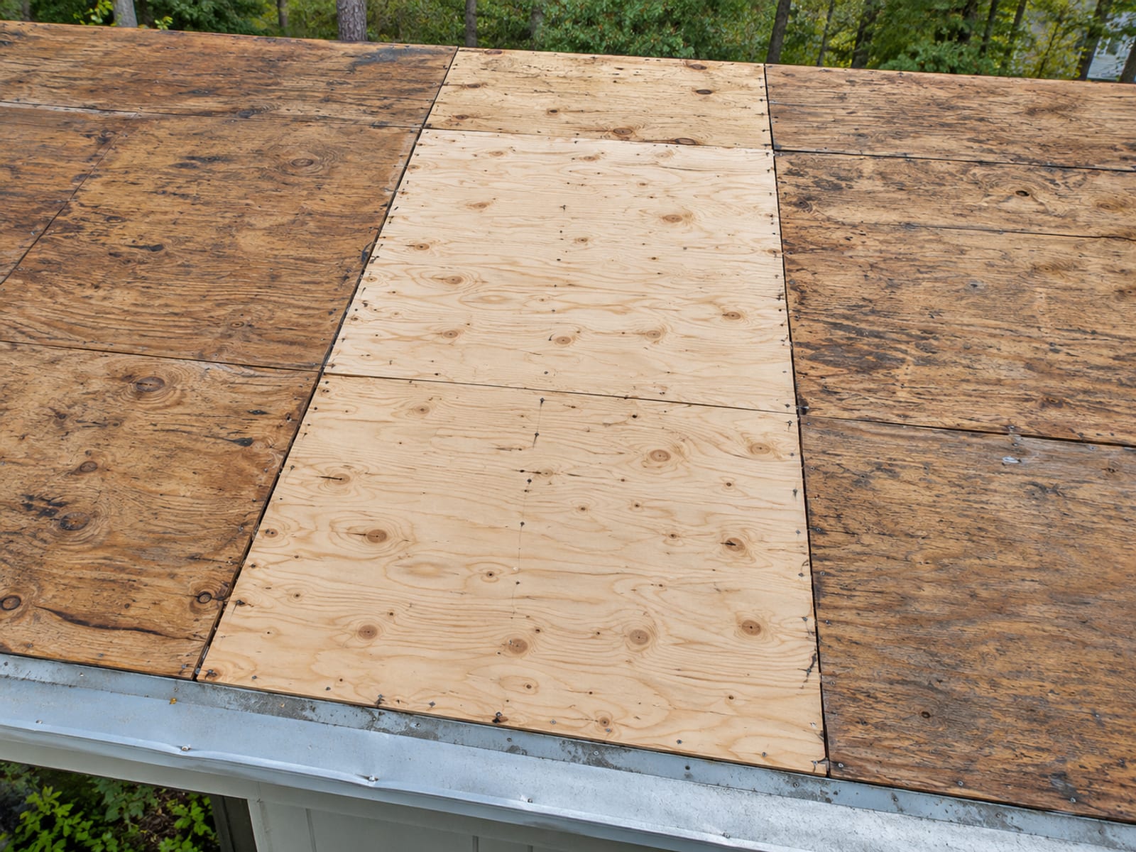 Top-down view of roof decking with a section of new light plywood sheathing fitted among older darker boards before the roof covering