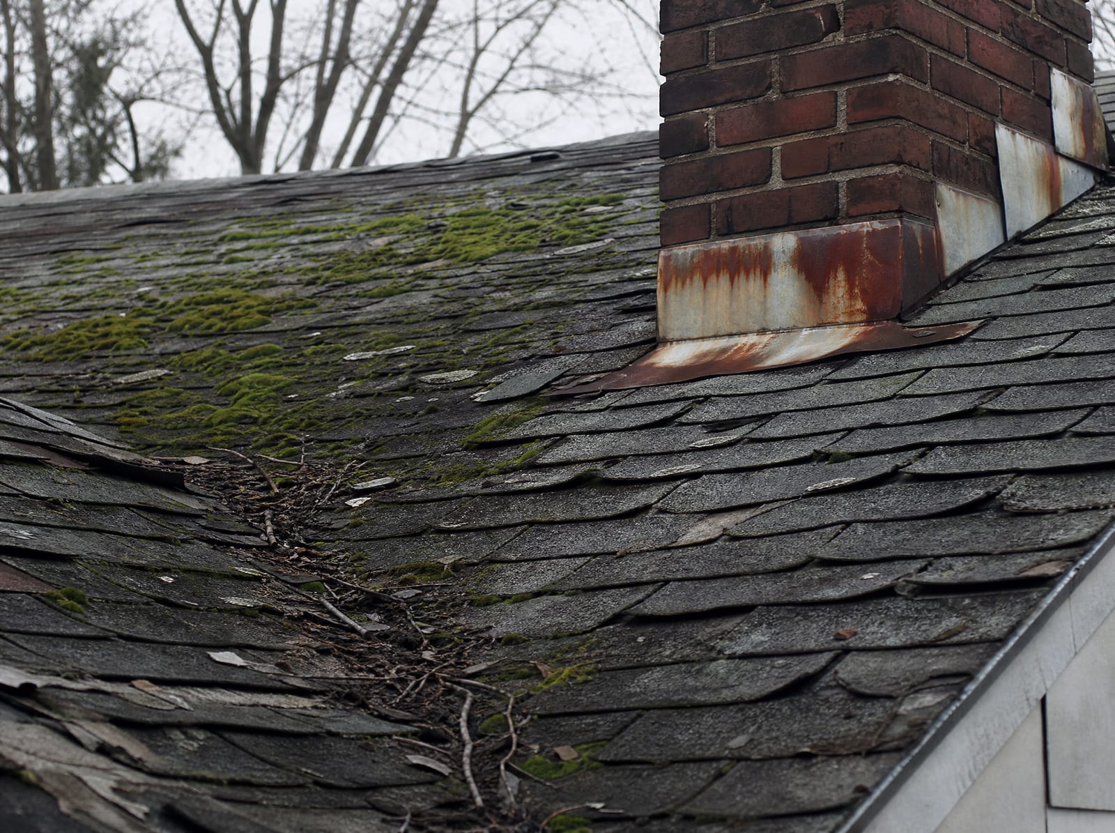 Aging asphalt shingle roof on an older Meriden home with moss on a shaded slope, granule loss, curling shingles, and rust-streaked chimney flashing