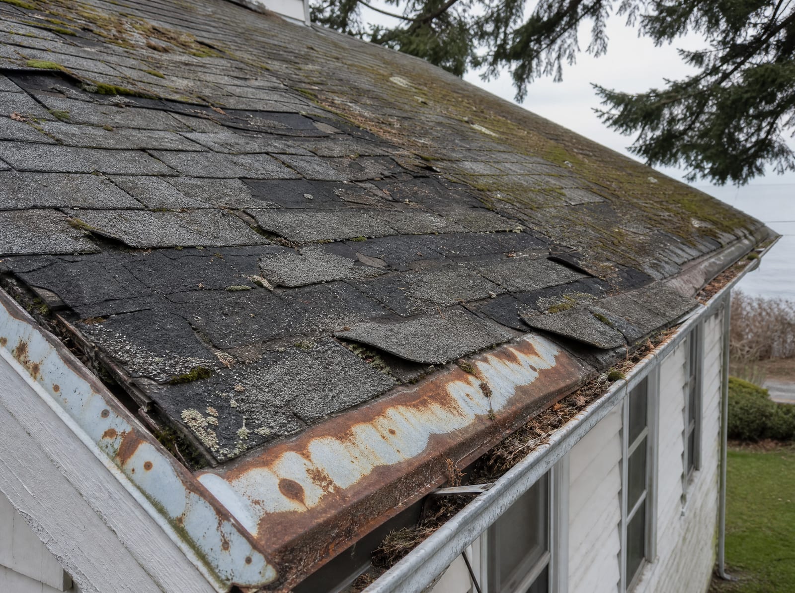 Aging asphalt shingle roof on an older coastal Cape home with granule loss, curling shingles, moss, and salt-corroded flashing