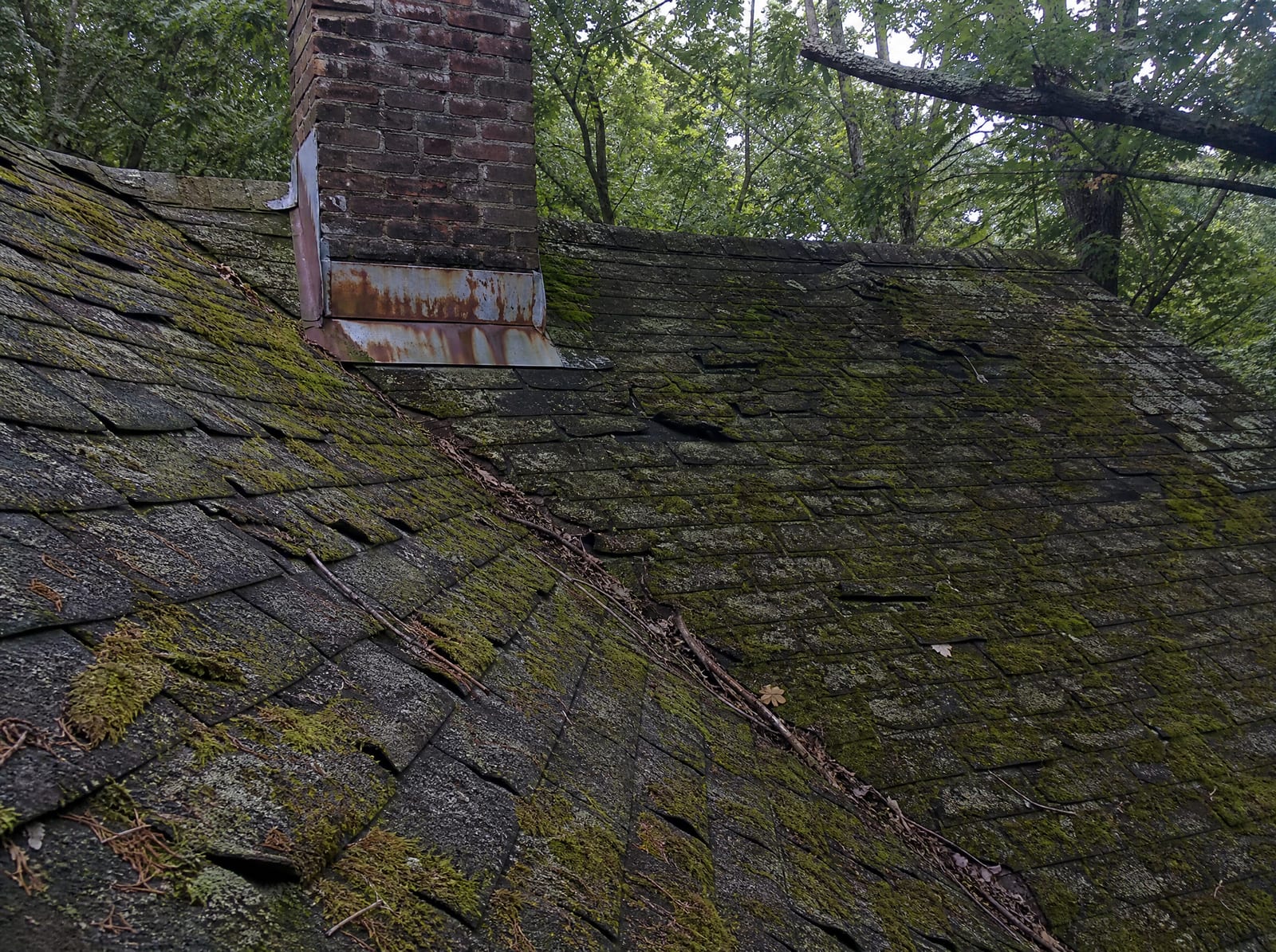 Aging asphalt shingle roof on an older Torrington home with moss on a shaded north slope, granule loss, curling shingles, and rust-streaked chimney flashing