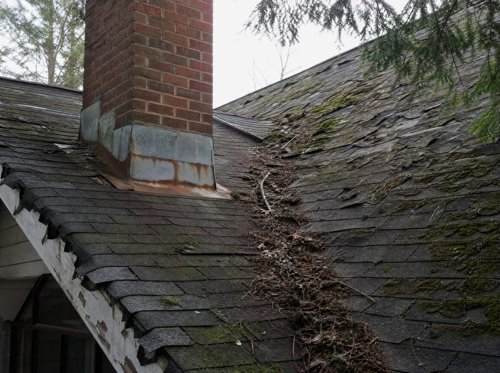 Aging asphalt shingle roof on an older Wallingford home with moss on a shaded slope, granule loss, curling shingles, and rust-streaked chimney flashing