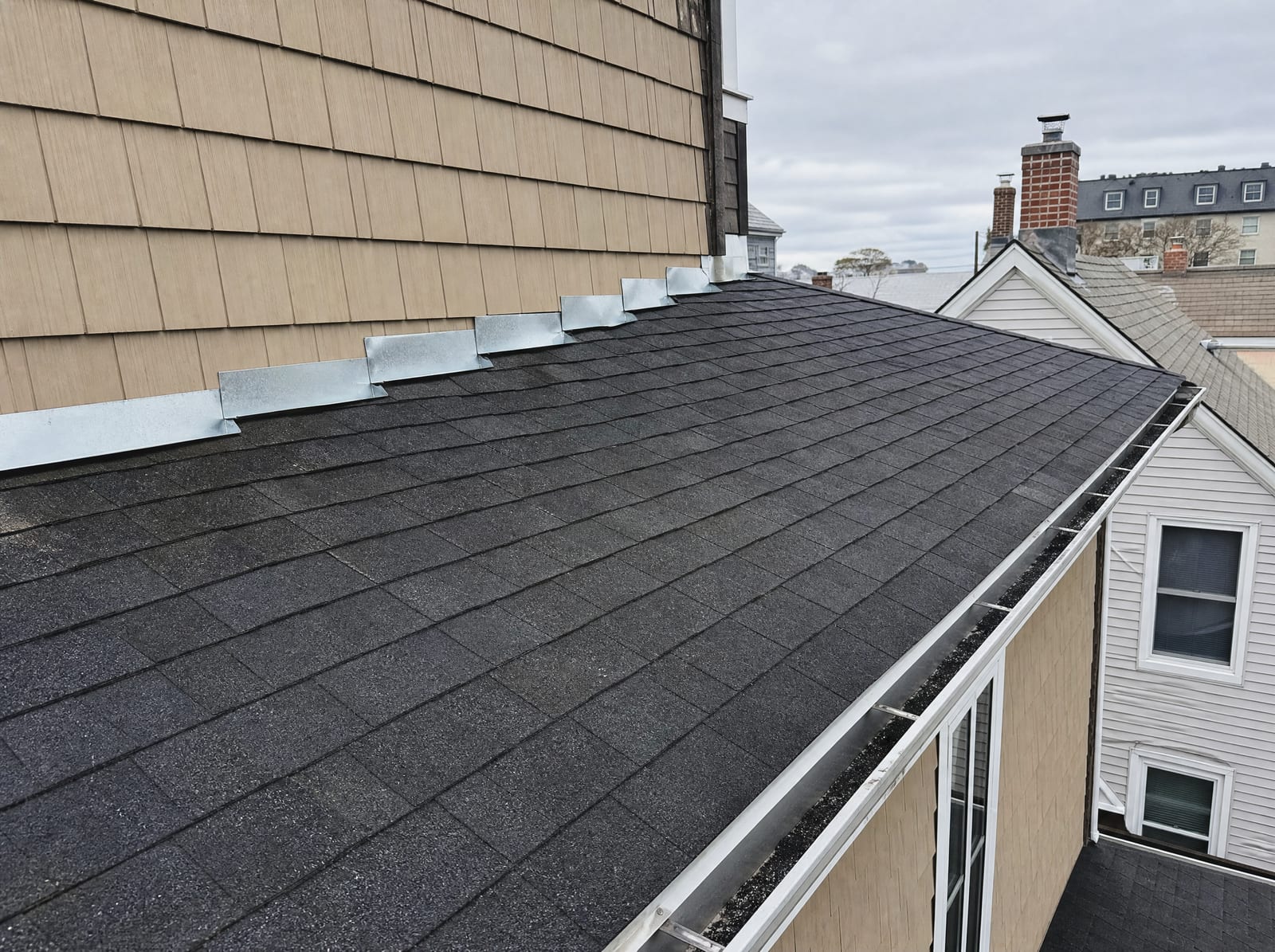 Freshly completed dark architectural asphalt shingle roof on an urban multi-family home with new step flashing, close to neighboring rooftops