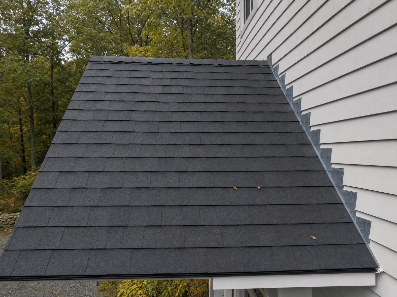 Freshly completed dark gray architectural asphalt shingle roof with clean straight shingle courses, new metal step flashing, and a continuous ridge vent