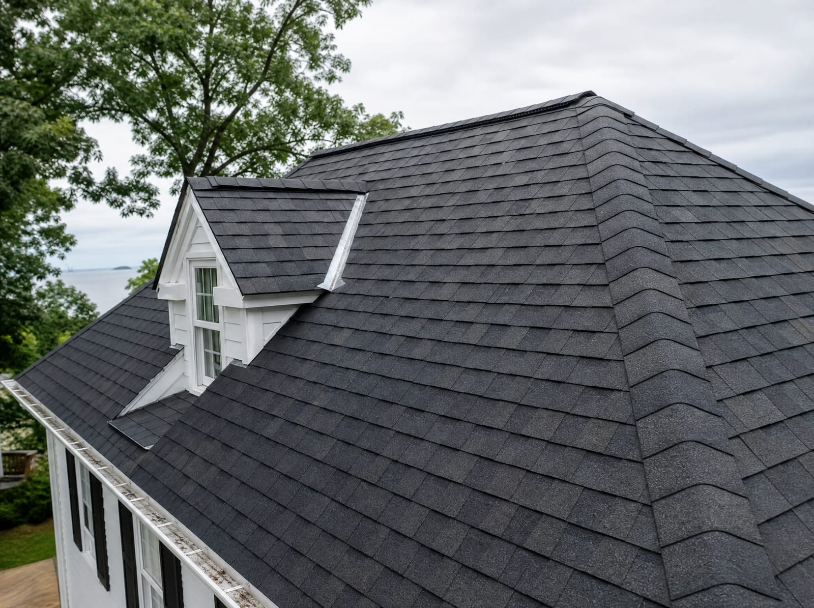 Freshly completed dark architectural asphalt shingle roof on a coastal New England colonial with new step flashing and a ridge vent