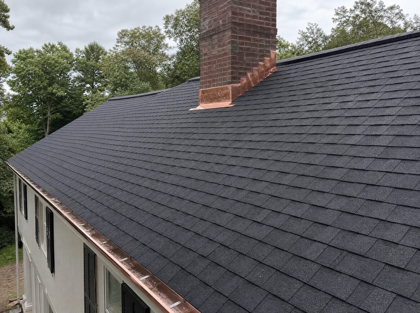 Freshly completed dark architectural asphalt shingle roof on a large colonial estate home with new copper-toned chimney flashing and a ridge vent