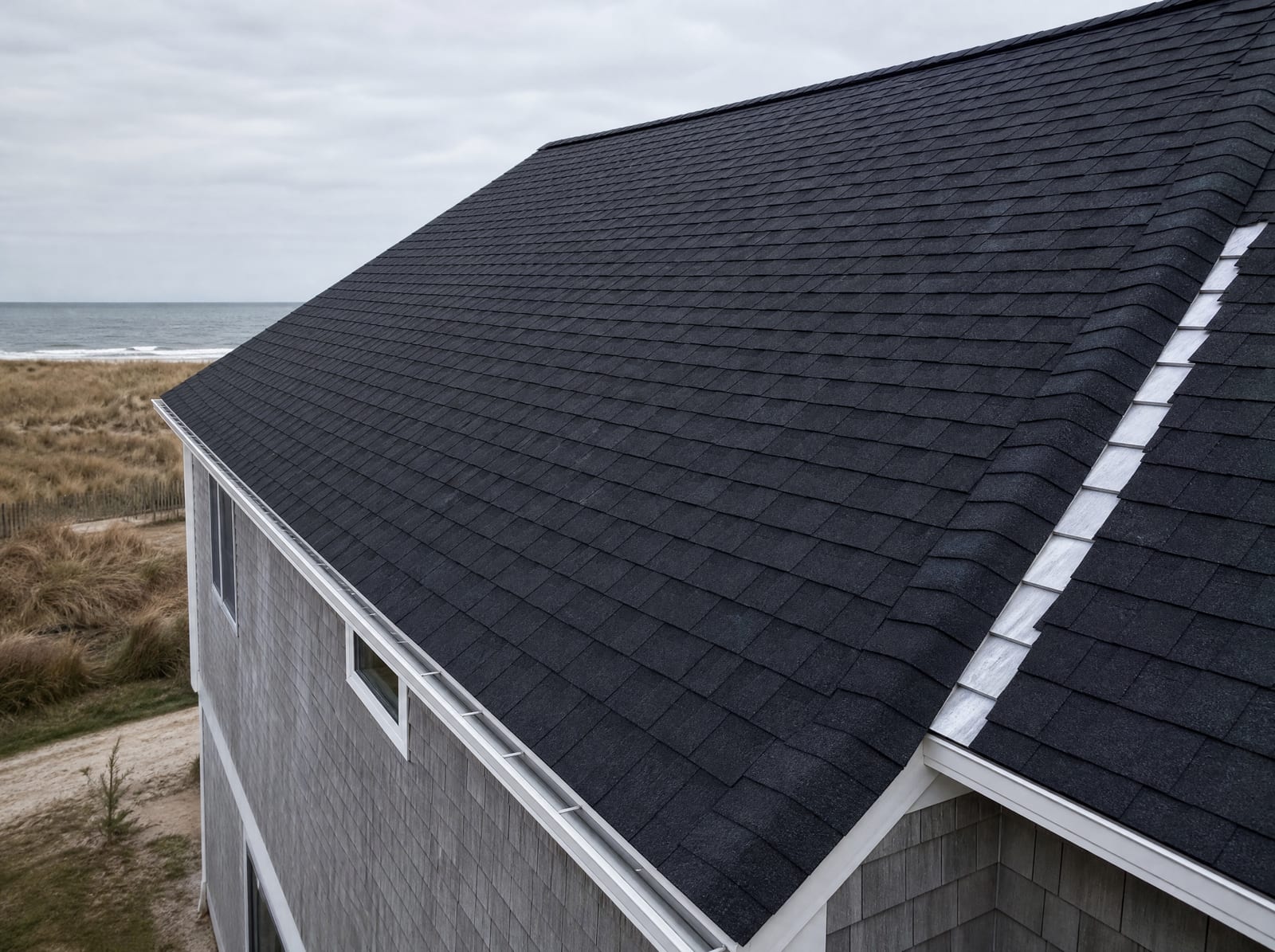 Freshly completed dark architectural asphalt shingle roof on a coastal Milford Cape home with corrosion-resistant step flashing and a ridge vent