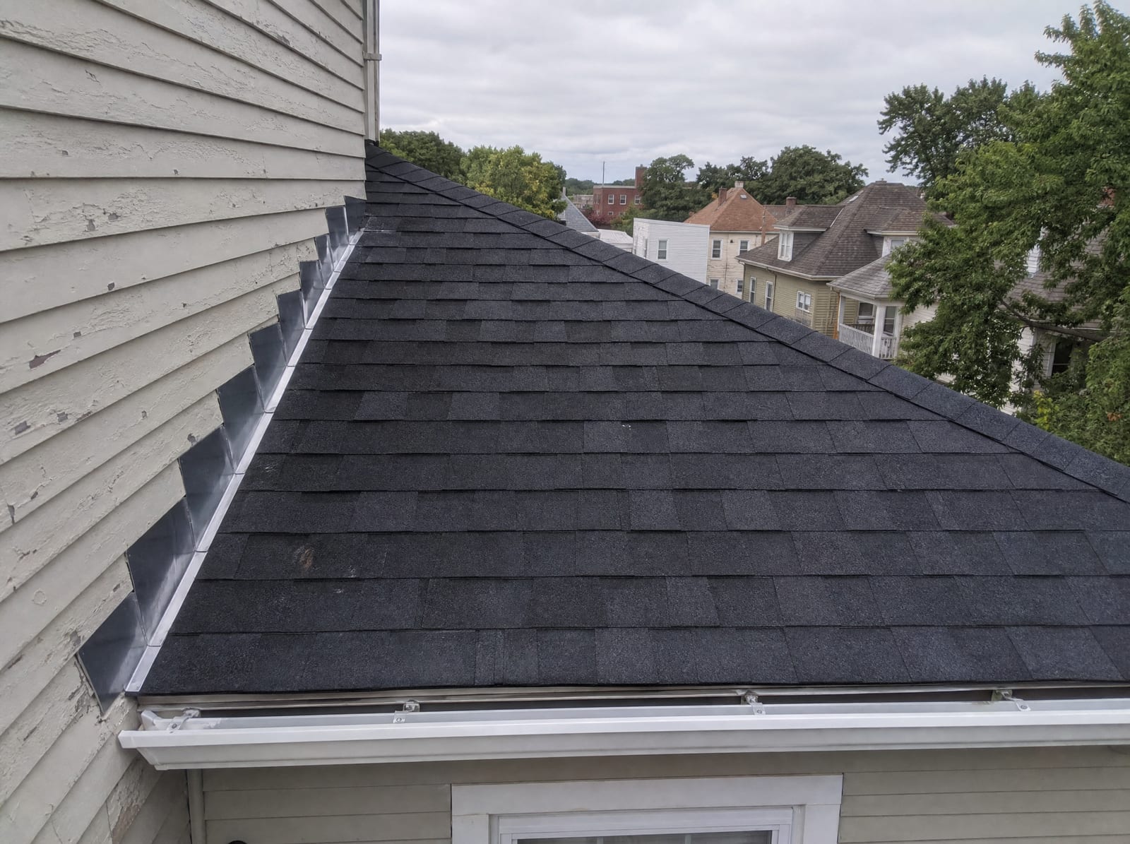 Freshly completed dark architectural asphalt shingle roof on an older New Haven multi-family home with new step flashing and a ridge vent