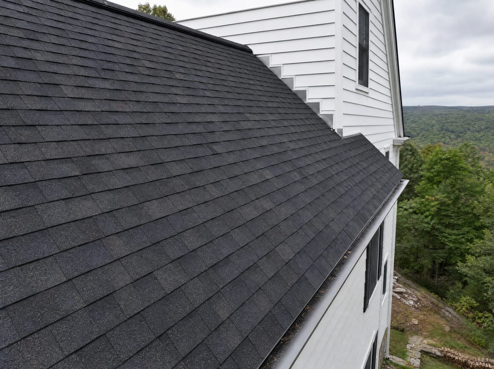 Freshly completed dark architectural asphalt shingle roof on an inland New England farmhouse with new step flashing and a ridge vent