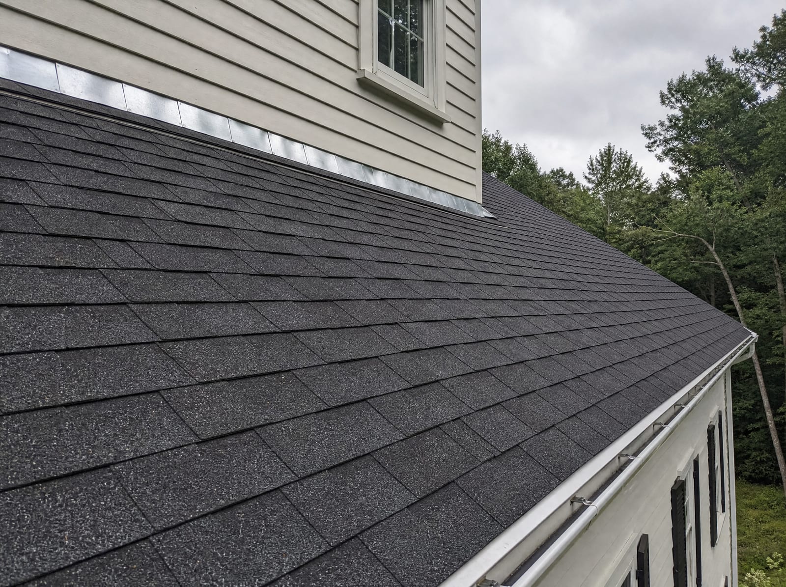 Freshly completed dark architectural asphalt shingle roof on a Newtown colonial farmhouse with new step flashing and a ridge vent