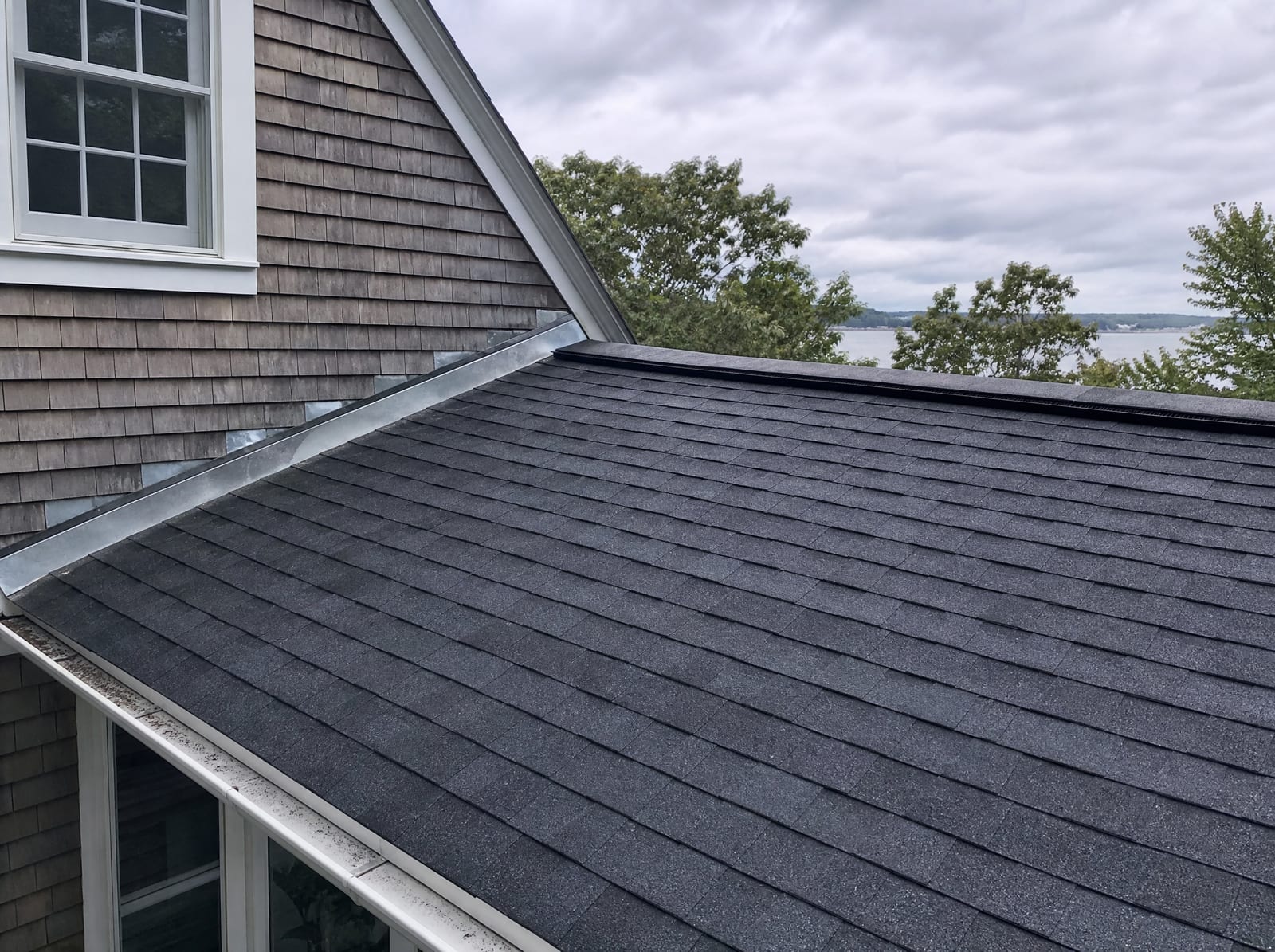 Freshly completed dark architectural asphalt shingle roof on a coastal New England colonial with new step flashing and a ridge vent