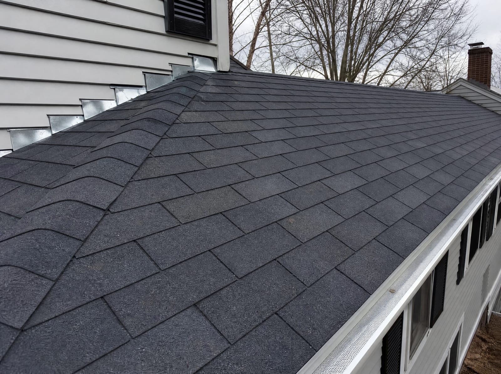 Freshly completed dark architectural asphalt shingle roof on a Southbury colonial home with new step flashing and a ridge vent
