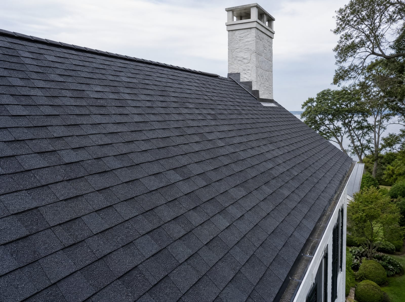 Freshly completed dark architectural asphalt shingle roof on a coastal colonial with new metal flashing and a ridge vent