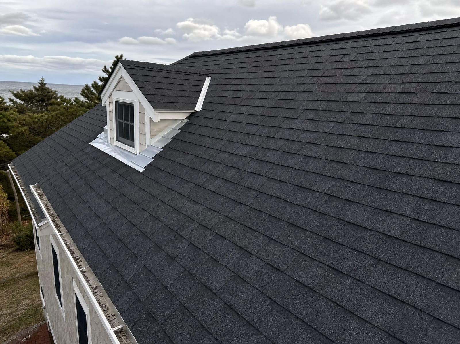 Freshly completed dark architectural asphalt shingle roof on a coastal Cape Cod home with new step flashing and a ridge vent