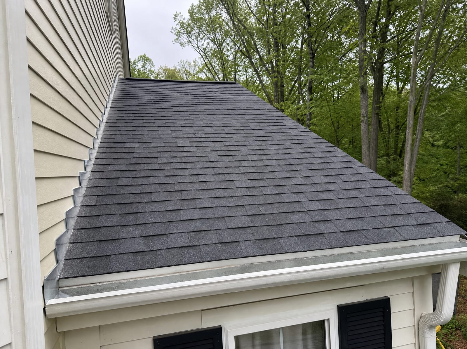Freshly completed dark architectural asphalt shingle roof on a wooded New England colonial home in Thomaston with new step flashing and a ridge vent