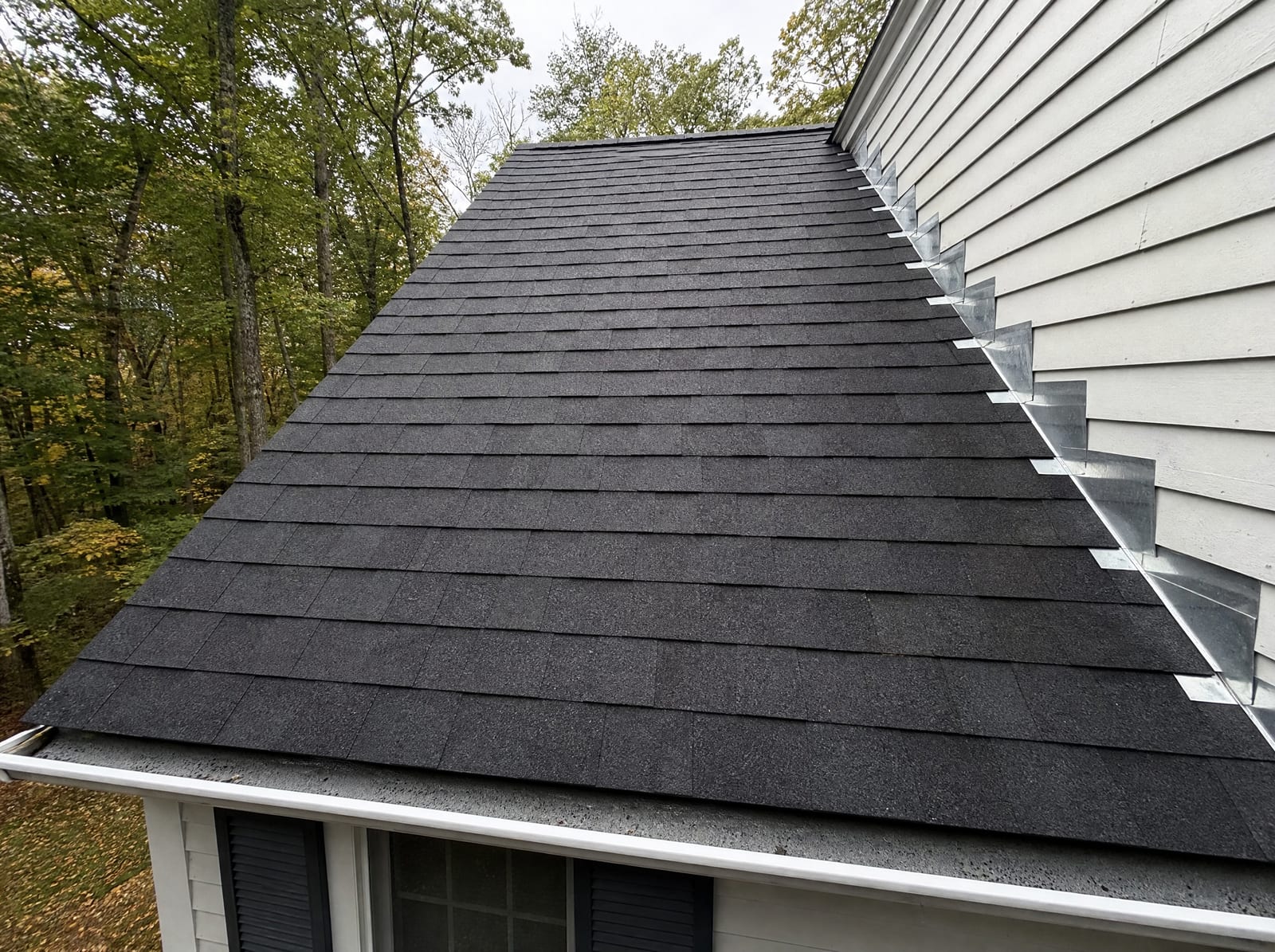 Freshly completed dark architectural asphalt shingle roof on a wooded New England colonial home in Torrington with new step flashing and a ridge vent