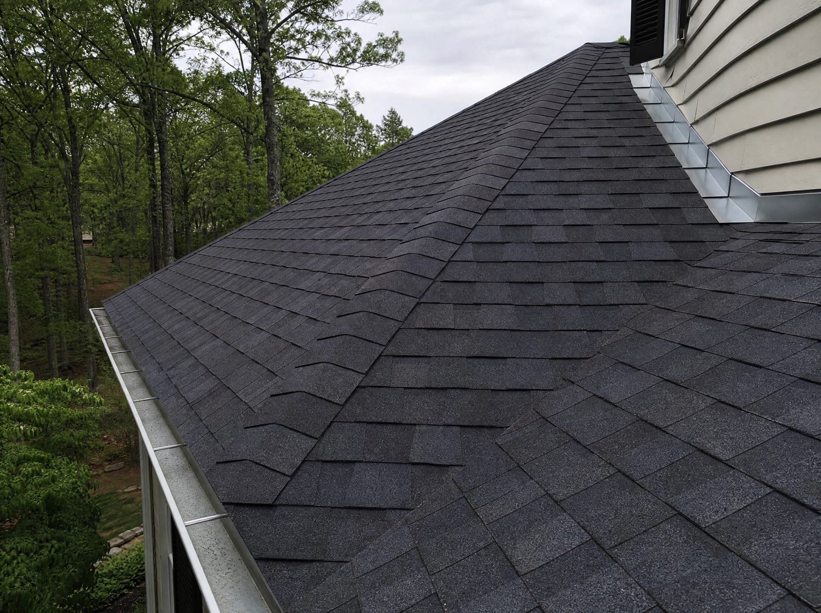 Freshly completed dark architectural asphalt shingle roof on a wooded New England colonial home in Watertown with new step flashing and a ridge vent