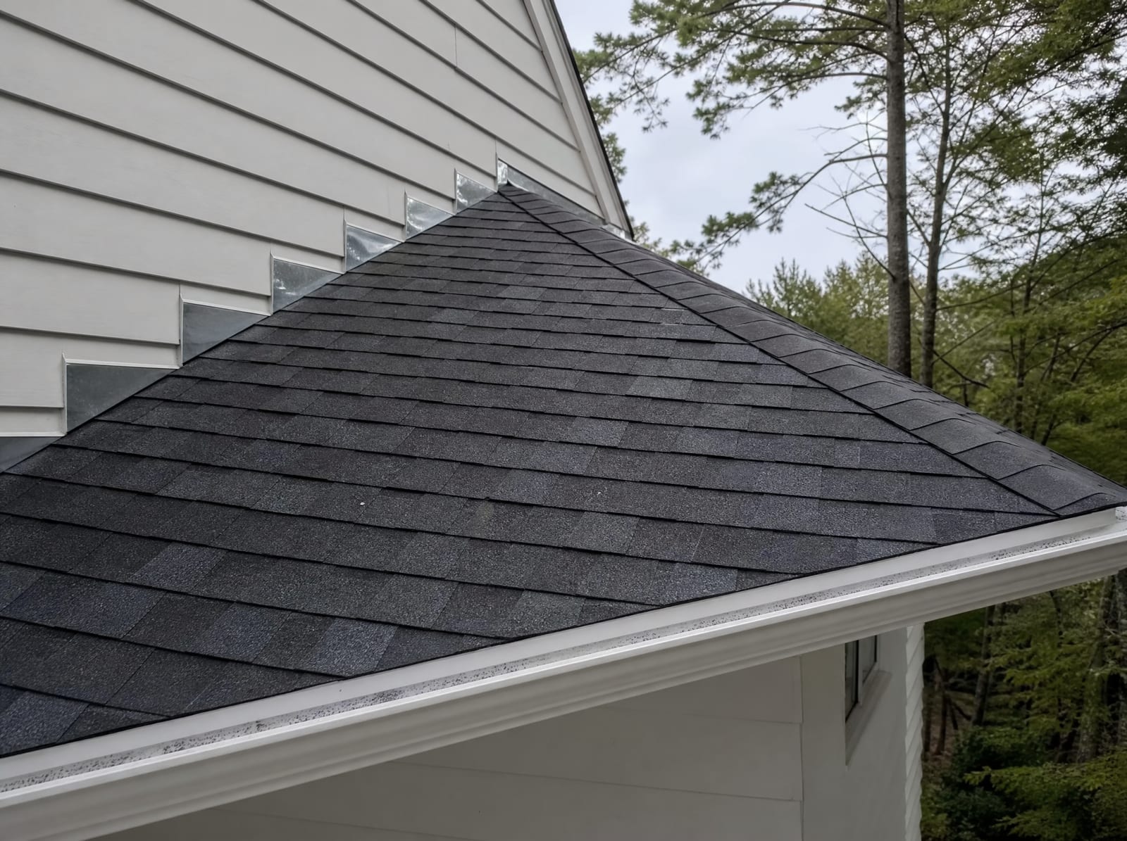 Freshly completed dark architectural asphalt shingle roof on a wooded colonial with new step flashing and a ridge vent