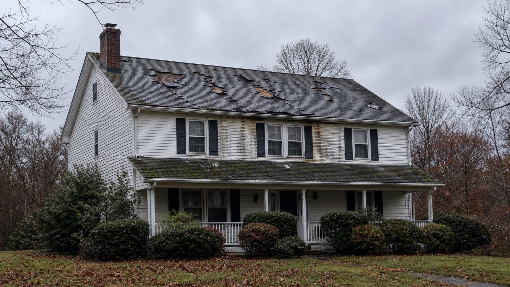 Close view of a residential skylight curb on a shingle roof showing deteriorated flashing and sealant at the uphill side of the skylight frame with dark water staining on the surrounding shingles