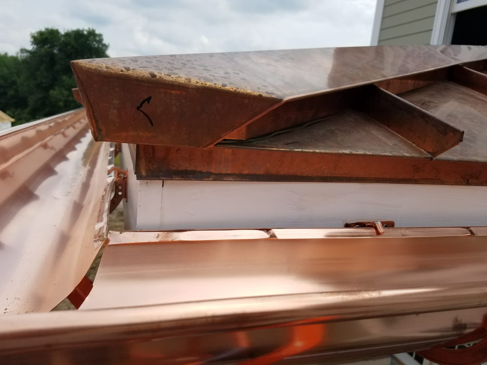 Newly installed shiny copper gutters mounted along a roofline next to aged copper flashing and drip edge on a residential home