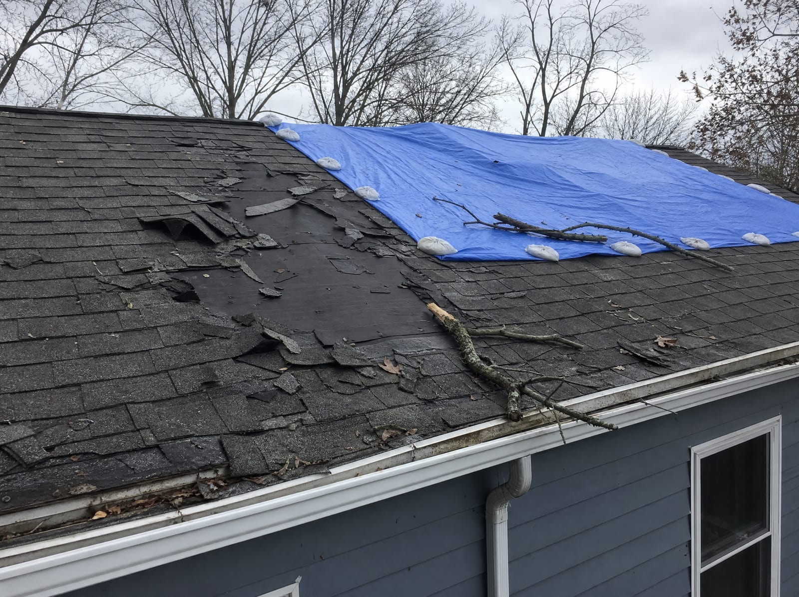 Storm-damaged Connecticut roof with lifted, torn shingles and a section covered by a secured blue emergency tarp